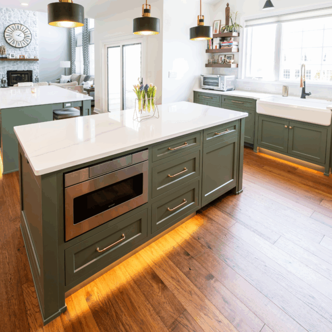 A kitchen with green cabinets by Laslo Custom Kitchens and black pendant lights.