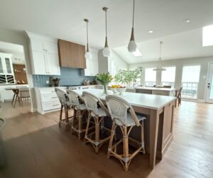 A kitchen with a large island, 4 white French barstools, and 3 lights.
