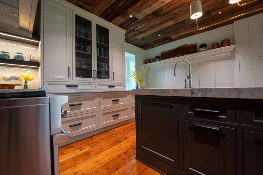 Custom kitchen renovation in Allentown with light inset cabinetry, a dark center island, and cabinetry fitted beneath the home's exposed wood ceiling, designed by Swine Design, LLC.