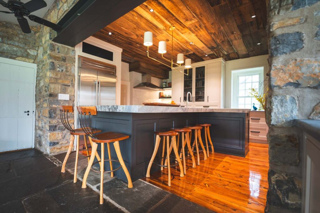 Rustic Lehigh Valley kitchen with a dark custom island, bar seating, stone walls, and a reclaimed wood ceiling.