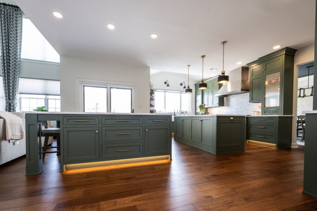 Double-island kitchen in Macungie, PA featuring dark green custom cabinetry, integrated storage, and toe-kick lighting.